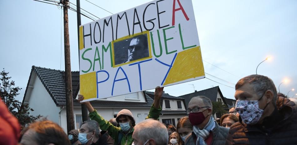 Un hombre sostiene un letrero que dice "Homenaje a Samuel Paty" durante la "Marche Blanche" el 20 de octubre de 2020, en Conflans-Sainte-Honorine, al noroeste de París, en solidaridad después de que un maestro fuera decapitado por mostrar a los alumnos caricaturas del profeta Mahoma. Foto vía AFP