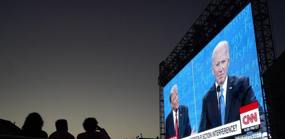 Varias personas siguen desde sus autos el debate presidencial entre el presidente, Donald Trump ( a la izquierda en la pantalla), y el aspirante demócrata, Joe Biden, en Fort Mason Center, San Francisco, el 22 de octubre de 2020. (AP Foto/Jeff Chiu)