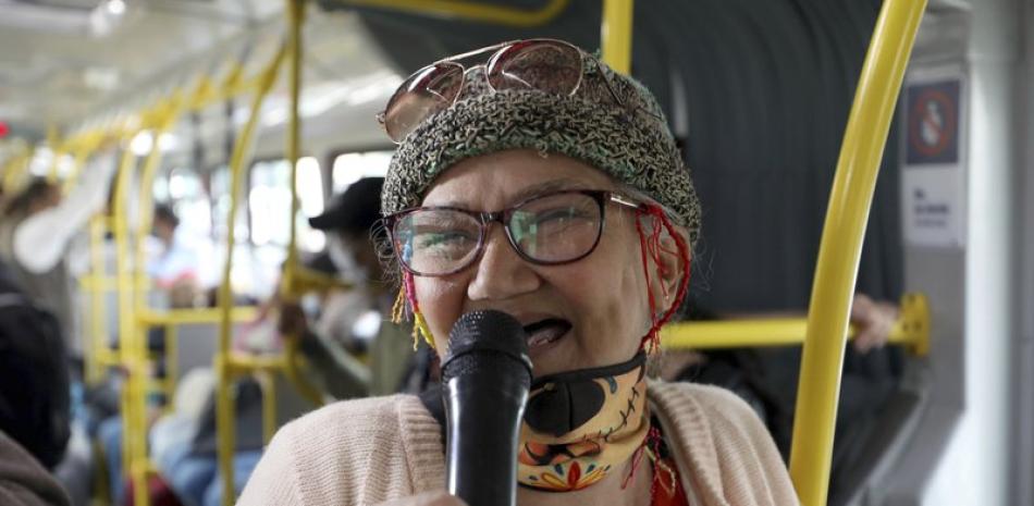 Marlene Alfonso, una abuela venezolana de 69 años que se hace llamar "Cindy sin dientes", canta sobre la vida de los migrantes de su país con la esperanza de recibir propinas de los viajeros en el Transmilenio, el sistema de autobuses públicos atestado y asotado por el crimen en Bogotá, el martes 3 de noviembre de 2020. (AP Foto/Fernando Vergara)