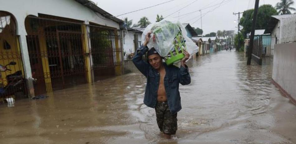 Un hombre camina por una calle anegada, con el agua a la altura de las rodillas, llevando sus pertenencias a cuestas, en San Manuel, Honduras, el 4 de noviembre de 2020. (AP Foto/Delmer Martínez)