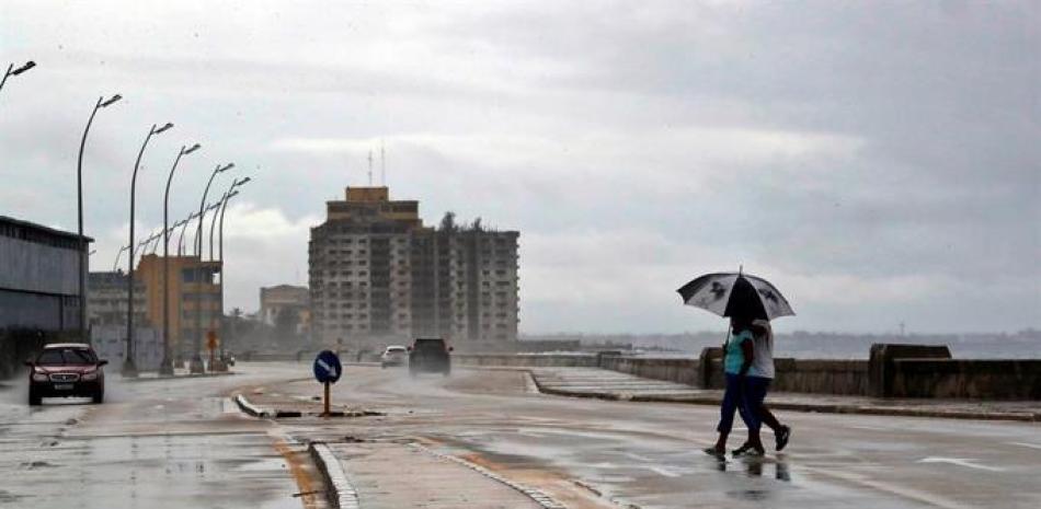 Dos personas protegidas con sombrilla por la lluvia cruzan la avenida del malecón tras el paso de Eta hoy, en la Habana (Cuba). EFE/ Ernesto Mastrascusa