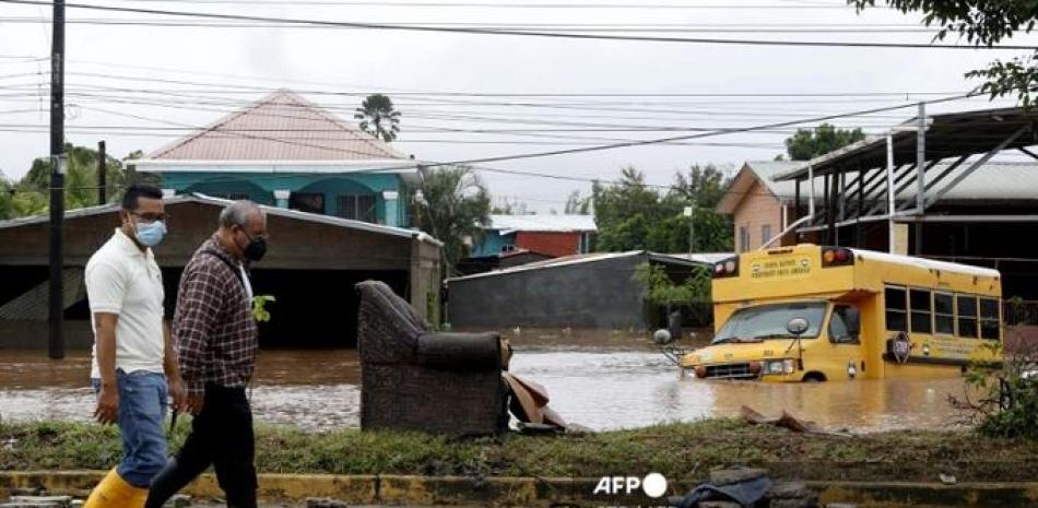 Hombres caminan por una zona inundada de El Progreso, en el departamento hondureño de Yoro, el 18 de noviembre de 2020 luego del paso del huracán Iota, ahora degradado a Tormenta Tropical.