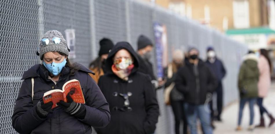 Ashley Gannon, izquierda, lee mientras espera en fila el jueves 19 de noviembre del 2020 afuera de un sitio de pruebas de coronavirus en Brooklyn, Nueva York. (AP Foto/Kathy Willens)
