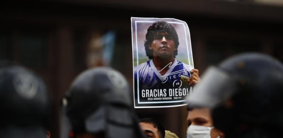 Un hombre sostiene un póster con la cara de Diego Maradona mientras espera en el exterior de la Casa Rosada para acceder a la capilla ardiente, en Buenos Aires, Argentina, el 26 de noviembre de 2020. (AP)