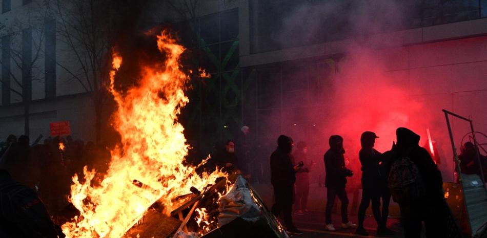 Los manifestantes se paran cerca de una barricada en llamas y una bengala roja durante una manifestación por los 'derechos sociales' y contra el proyecto de ley de 'seguridad global'.