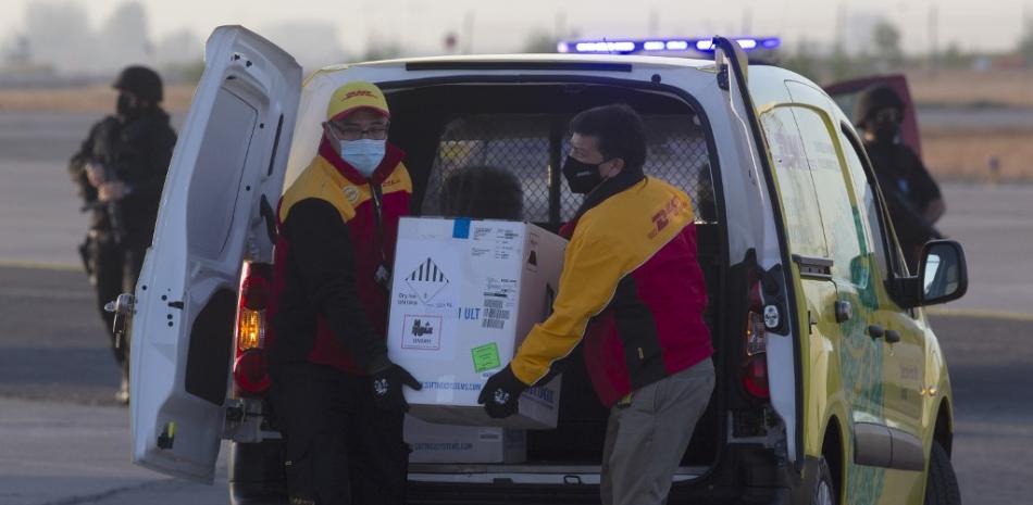 Los trabajadores llevan una caja que contiene la vacuna contra el coronavirus Pfizer-BioNTech COVID-19 a un helicóptero para su distribución en el aeropuerto internacional de Santiago el 24 de diciembre de 2020. Claudio Reyes / AFP
