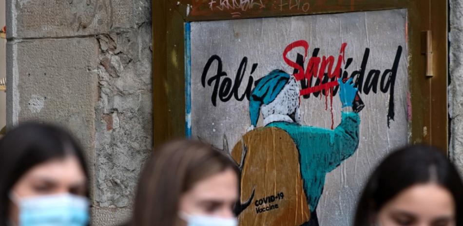 La gente pasa junto a un nuevo trabajo del artista callejero italiano TvBoy que representa a Santa Claus llevando la vacuna Covid-19 en su saco, en Barcelona el 24 de diciembre de 2020. Josep Lago / AFP