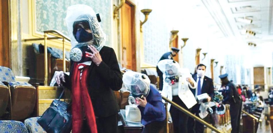 Congresistas con máscaras antigases se retiran, durante el asalto an Capitolio estadounidense antier. AP