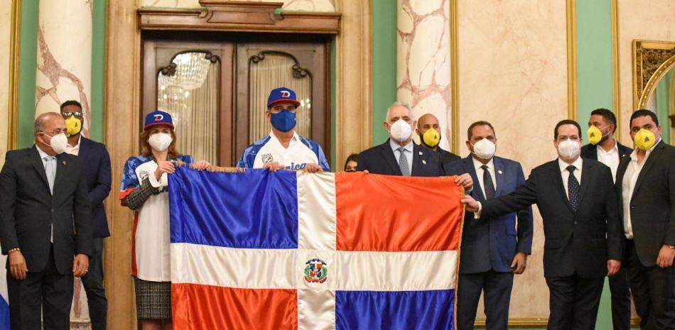 El presidente Luis Abinader y la vicepresidenta Raquel Peña, junto a Vitelio Mejía sostienen la bandera dominicana, acompañados de ejecutivos del equipo de las Águias Cibaeñas, el Ministro de Salud, doctor Plutarco Arias y el Comisionado Nacional de Béisbol, Junior Arias Noboa.