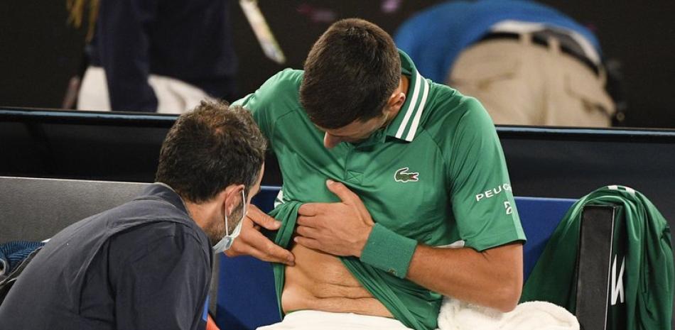 Novak Djokovic le muestra a un médico la zona donde se lesionó durante su partido con Taylor Fritz por la tercera ronda del Abierto Australiano este viernes, en Melbourne. El serbio ganó en cinco sets, pero dice que no sabe si podrá continuar en el torneo. "Estoy seguro de que es un tirón", declaró.