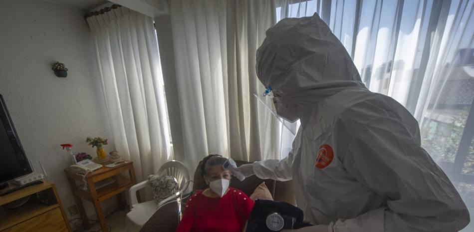 Karla Hitzuri Montano, cirujana médica, vestida con traje de protección, mide la temperatura de su paciente Rosario Socorro de 70 años./ AFP
