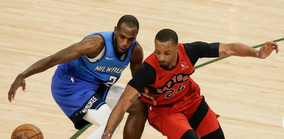 Khris Middleton de los Bucks de Milwaukee y Norman Powell de los Raptors de Toronto van tras un balón suelto durante la primera mitad de un juego de baloncesto de la NBA este jueves.