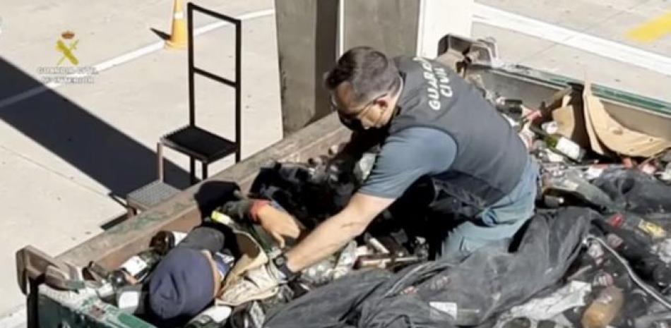 Imagen tomada de un video proporcionado por la Guardia Civil de un agente de la Guardia Civil ayudando a un hombre a salir de entre botellas de vidrio en un contenedor en Melilla, España, el viernes 19 de febrero de 2021. (Guardia Civil vía AP)