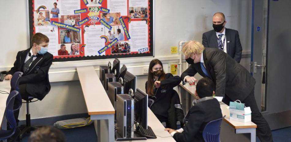El primer ministro británico, Boris Johnson, a la derecha, choca el codo de una alumna de 7mo año durante una visita a la Academia Accrington en Accrington, Inglaterra, el jueves 25 de febrero de 2021, que se está preparando para el regreso de los alumnos el 8 de marzo. (Anthony Devlin/Pool Foto via AP)