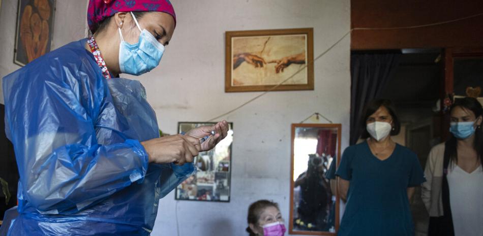 Una trabajadora de la salud prepara una dosis de la vacuna para el COVID-19 de Sinovac Biotech de China mientras Filomena Zuleta, de 70 años, espera ser inoculada en la casa de su familia en Santiago, Chile, el jueves 25 de febrero de 2021.

Foto: AP/Esteban Felix