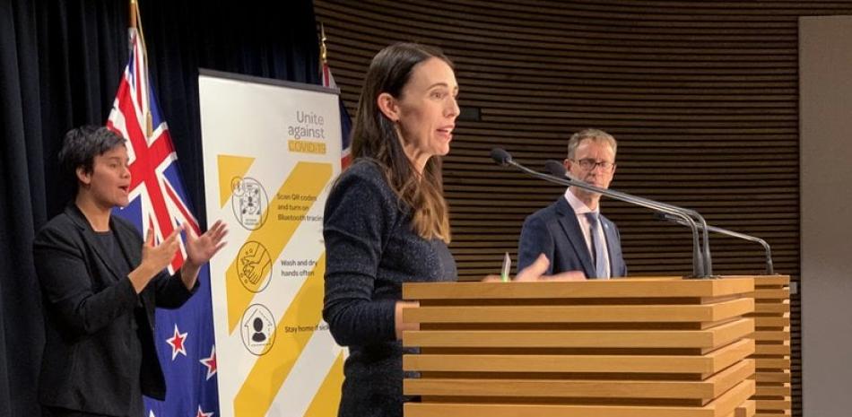 La primera ministra de Nueva Zelanda, Jacinda Ardern, en el centro, y el director general de salud, Ashley Bloomfield, a la derecha, hablan con los medios en Wellington, Nueva Zelanda, el lunes 15 de febrero de 2021. (AP Foto/Nick Perry)