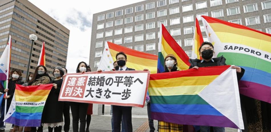 Abogados de los demandantes y partidarios posan con banderas arco iris, símbolo de la comunidad LGBTQ, y un cartel con el lema "Fallo inconstitucional" en el exterior del tribunal de distrito de Sapporo tras un juicio, en Sapporo, en el norte de Japón, el 17 de marzo de 2021. (Yohei Fukai/Kyodo News via AP)
