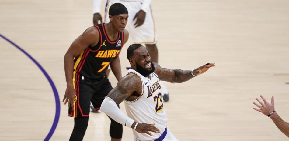 El alero de Los Angeles Lakers, LeBron James, centro, hace una mueca cuando tropieza y se lesiona por el alero de los Atlanta Hawks, Tony Snell, abajo, durante la primera mitad de un partido de baloncesto de la NBA el sábado 20 de marzo de 2021 en Los Ángeles.