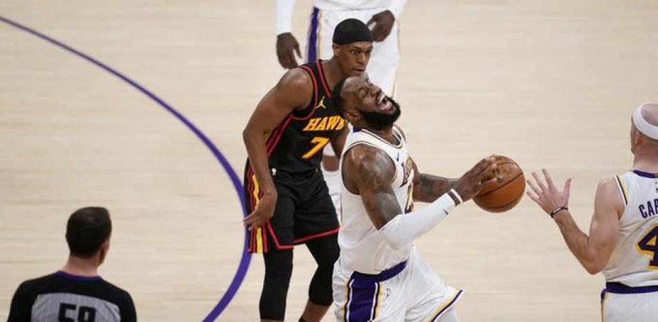 El alero de Los Angeles Lakers, LeBron James, centro, hace una mueca cuando tropieza y se lesiona por el alero de los Atlanta Hawks, Tony Snell, abajo, durante la primera mitad de un partido de baloncesto de la NBA este sábado 20 de marzo de 2021 en Los Ángeles.