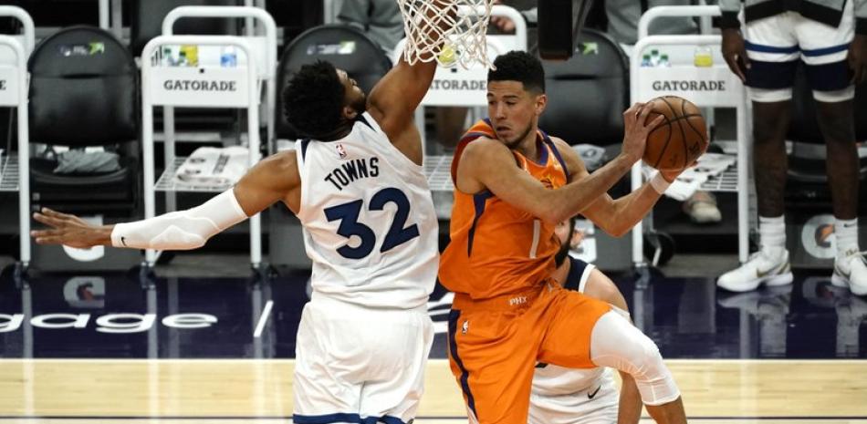 El escolta de los Phoenix Suns, Devin Booker (1), busca pasar el balón alrededor del centro de los Minnesota Timberwolves, Karl-Anthony Towns (32), durante la segunda mitad de un juego de baloncesto de la NBA este viernes en Phoenix.