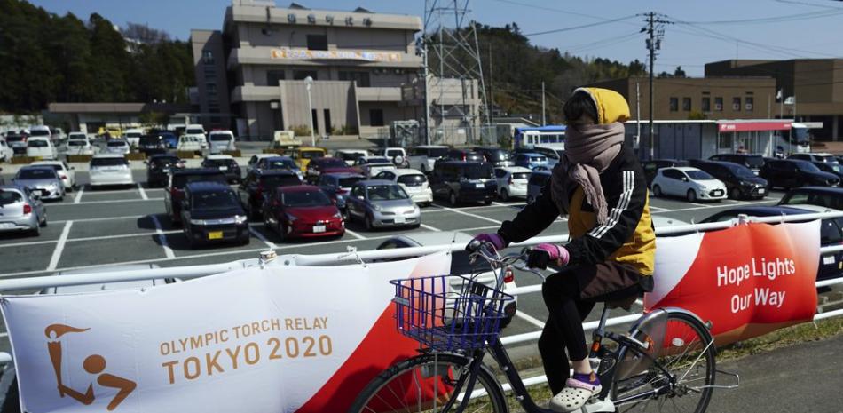 Una mujer pedalea frente a carteles con el logo del relevo de la antorcha olímpica en Naraha, Japón, este miércoles 24 de marzo de 2021.