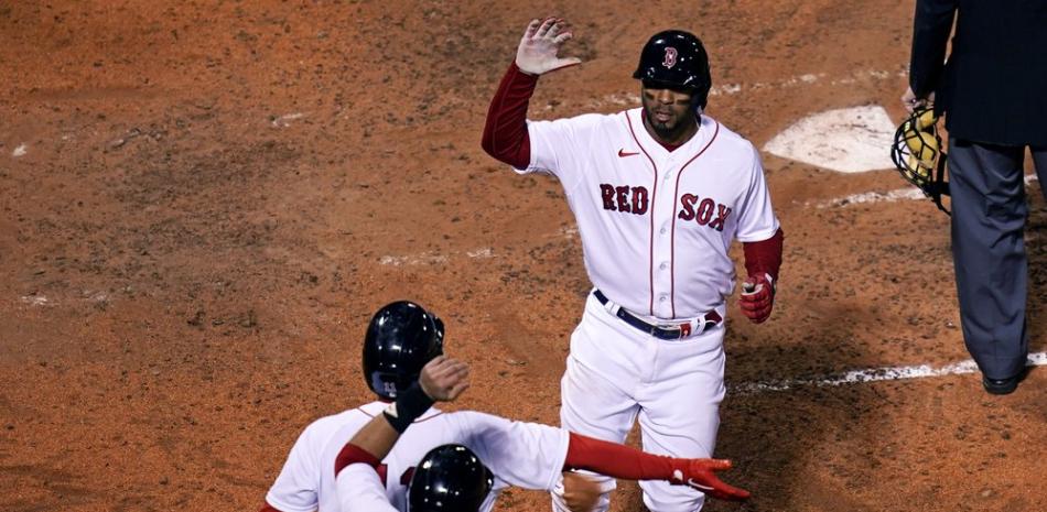 Xander Bogaerts, de los Medias Rojas de Boston, arriba, es felicitado por Rafael Devers, centro, y JD Martínez (28) luego de anotar en su propio doble luego de un error de lanzamiento del receptor de los Tampa Bay Rays Mike Zunino, durante la quinta entrada de un juego de béisbol en Fenway Park, este  lunes, en Boston.
