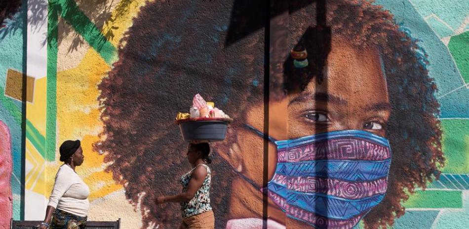Dos mujeres caminan frente a un mural alusivo al uso del tapabocas por el coronavirus en Puerto Príncipe (Haití). EFE/ Orlando Barría/Archivo