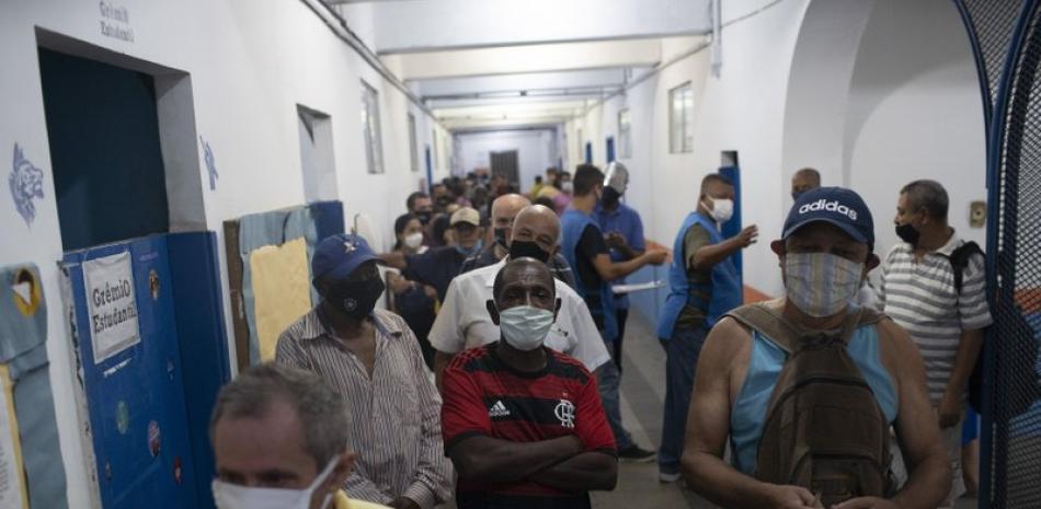 Personas con sus cubrebocas por la pandemia de coronavirus hacen fila para votar en las elecciones municipales en un centro de votación en el barrio pobre de Rocinha, en Río de Janeiro, Brasil, el domingo 15 de noviembre de 2020.

Foto: AP/Silvia Izquierdo