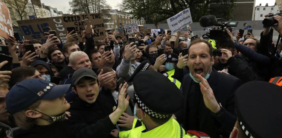 El exarquero del Chelsea, Petr Cech (derecha), detrás de un grupo de policías, trata de calmar a hinchas que protestan en Londres contra la creación de la Superliga europea.