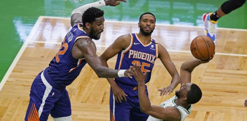 El base de los Celtics de Boston Kemba Walker lanza el balón y anota mientras trastabilla y lo defiende Deandre Ayton y Mikal Bridges de los Suns de Phoenix el jueves 22 de abril del 2021.