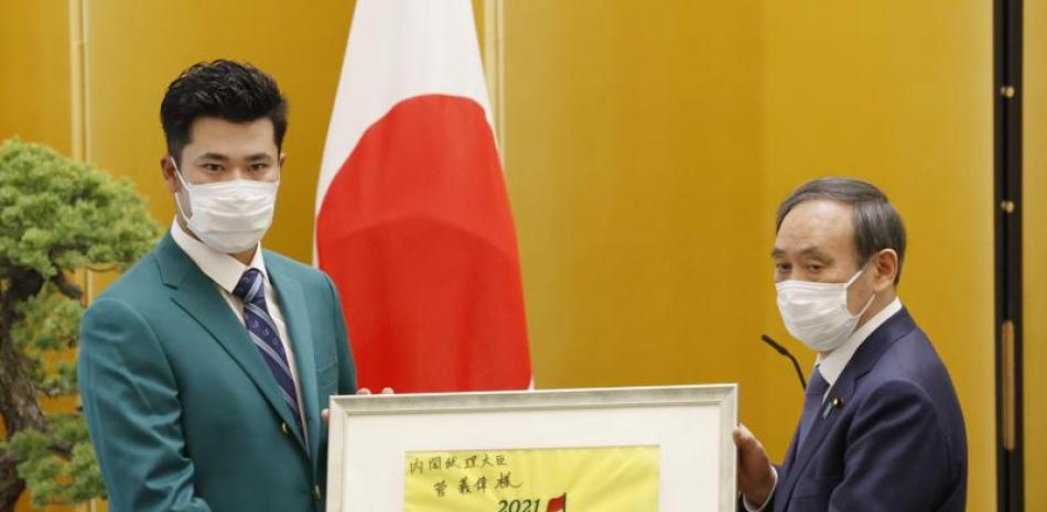 El golfista japonés Hideki Matsuyama, izquierda, entrega un regalo al primer ministro Yoshihide Suga en la oficina del mandatario en Tokio, el viernes 30 de abril de 2021. (Masanori Takei/Kyodo News vía AP).