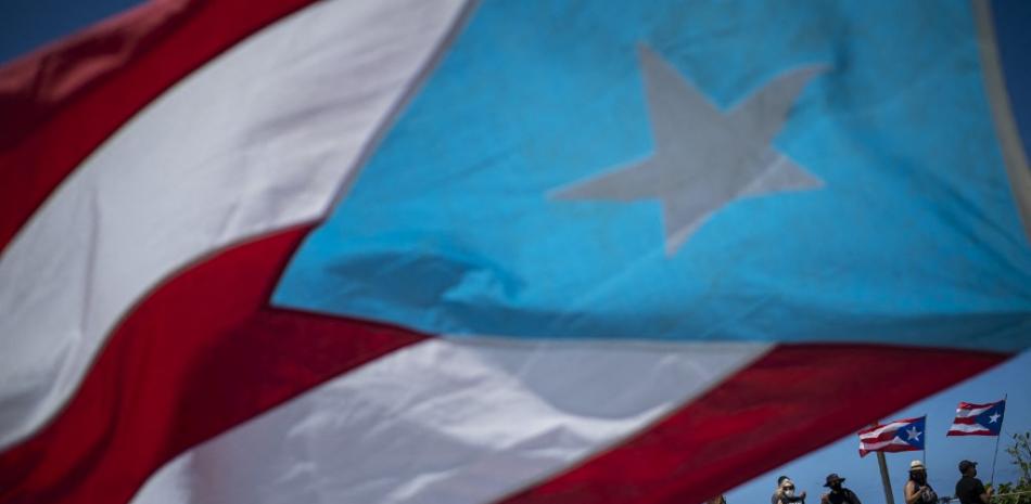 Las personas ondean banderas mientras participan en una manifestación para conmemorar el Primero de Mayo, o Día Internacional de los Trabajadores, en San Juan, Puerto Rico, el 1 de mayo de 2021. Ricardo ARDUENGO / AFP
