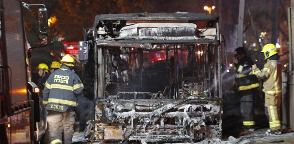 Los bomberos israelíes revisan un autobús quemado en la ciudad israelí de Holon, cerca de Tel Aviv, el 11 de mayo de 2021, después de que se lanzaran cohetes hacia Israel desde la Franja de Gaza controlada por el movimiento palestino Hamas. Ahmad GHARABLI / AFP