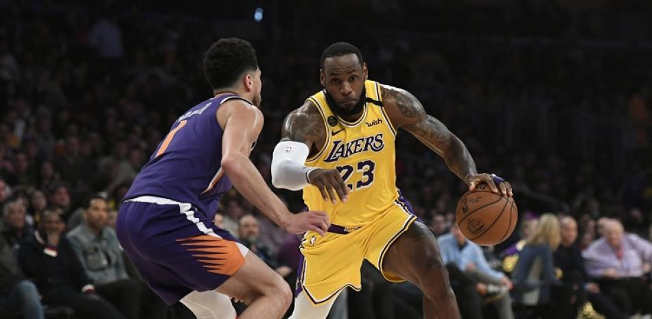 LeBron James, de los Lakers, enfrente la defensa de Devin Booker, de los Suns, en acción de un partido del baloncesto de la NBA.