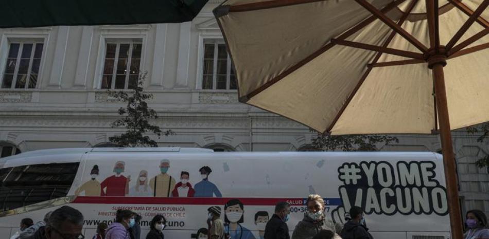 La gente almuerza en un restaurante que tiene mesas en la calle como medida para frenar la propagación del nuevo coronavirus frente a un autobús móvil de vacunación en Santiago, Chile, el lunes 24 de mayo de 2021. (Foto AP/Esteban Félix)