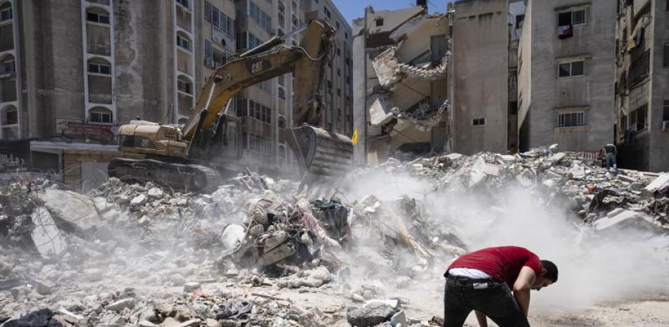 Equipo pesado de construcción es utilizado para revisar entre los escombros de un edificio destruido por un ataque aéreo durante los enfrentamientos entre el grupo Hamas, que gobierna Gaza, e Israel, el jueves 27 de mayo de 2021 en Ciudad de Gaza. (AP Foto/John Minchillo