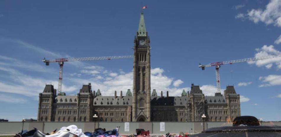 Zapatos, letreros y tabaco son colocados frente al Parlamento, en Ottawa, Ontario, el lunes 31 de mayo de 2021, en reconocimiento al descubrimiento de los cadáveres de decenas de niños en el sitio de un antiguo internado en Kamloops, Columbia Británica. (Adrian Wyld/The Canadian Press via AP