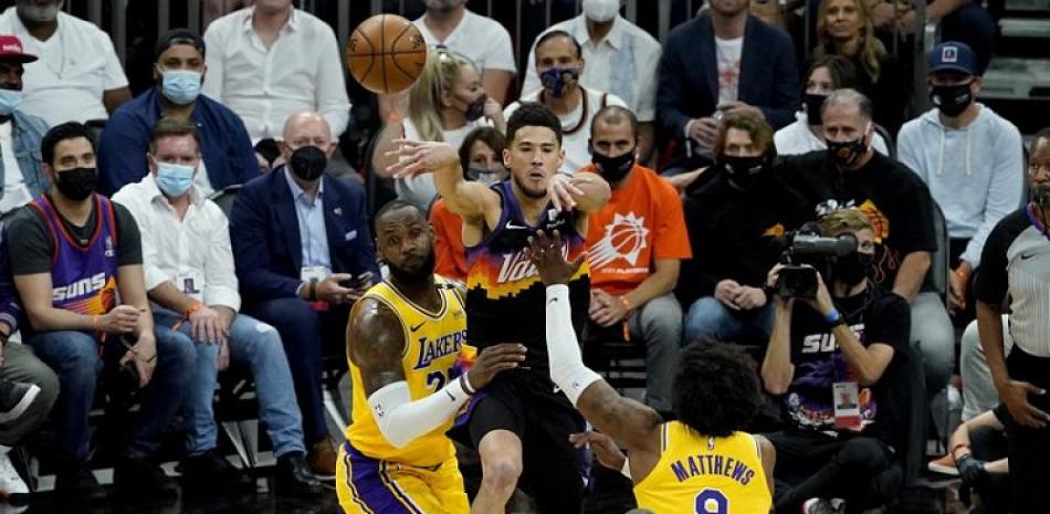 Devin Booker, de Phoenix, pasa el balón por encima de LeBron James y Wesley Matthews, de los Lakers, en la primera mitad del quinto partido de su serie.