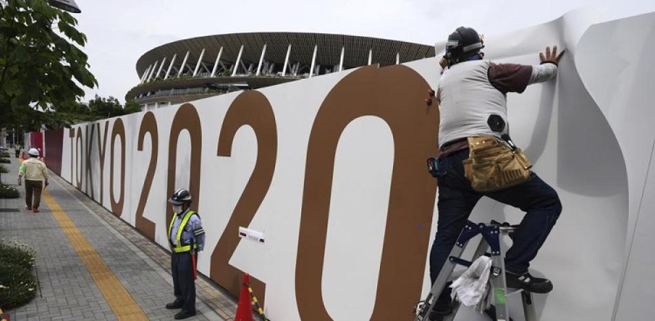 Obreros colocan logos en una barrera frente al Estadio Nacional, sede de la ceremonia de apertura y otras competencias de los Juegos Olímpicos de Tokio.