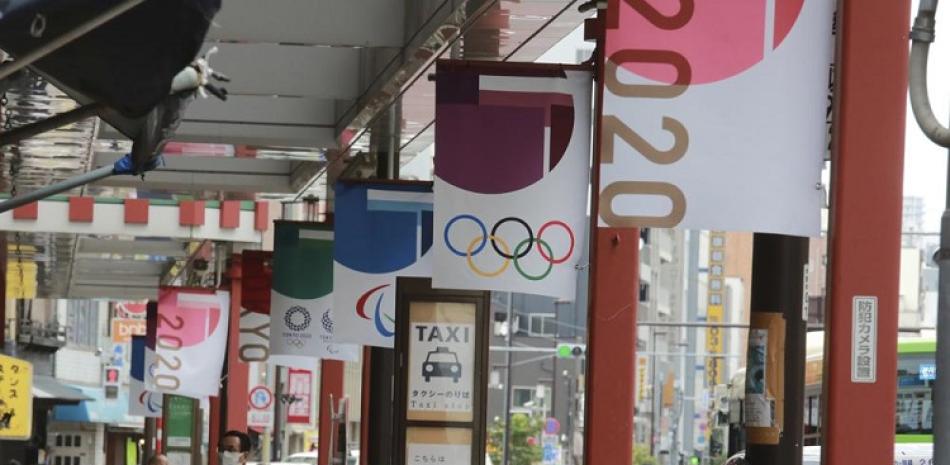 Personas con mascarillas contra el coronavirus caminan bajo un pancarta de los Juegos Olímpicos de Tokio 2020.