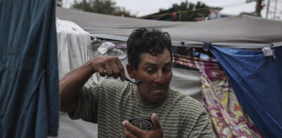 El migrante hondureño Christian Fragoso sostiene un espejo en una mano mientras se afeita la cara en un campamento de migrantes cerca del puente peatonal fronterizo El Chaparral en Tijuana, México, el viernes 2 de julio de 2021. (AP Photo/Emilio Espejel)