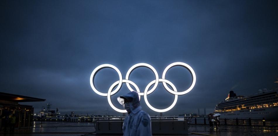 Un hombre pasa junto a los Anillos Olímpicos iluminados al anochecer en Yokohama el 2 de julio de 2021. Philip FONG / AFP