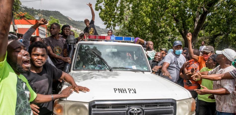 La gente vitorea cuando un coche de policía pasa por la comisaría de Petionville, donde hombres armados, acusados de estar involucrados en el asesinato del presidente Jovenel Moise, están detenidos en Puerto Príncipe el 8 de julio de 2021. La policía de Haití ha rodeado a un grupo de posibles sospechosos en el asesinato del presidente Jovenel Moise, dijo el enviado de la ONU a Haití.  Valerie Baeriswyl / AFP