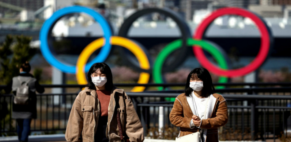 Las personas con máscaras faciales protectoras, después de un brote del coronavirus, se ven frente a los anillos olímpicos gigantes en la zona costera del Parque Marino Odaiba en Tokio, Japón, el 27 de febrero de 2020. © Athit Perawongmetha / Reuters