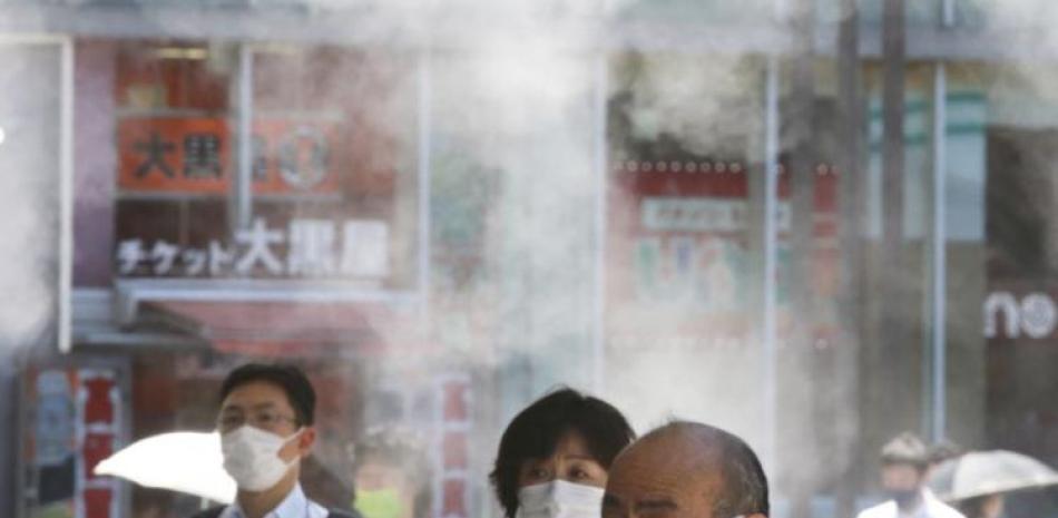 Gente con mascarillas para protegerse contra la expansión del coronavirus caminan bajo agua vaporizada en Tokio, el jueves 5 de agosto de 2021.