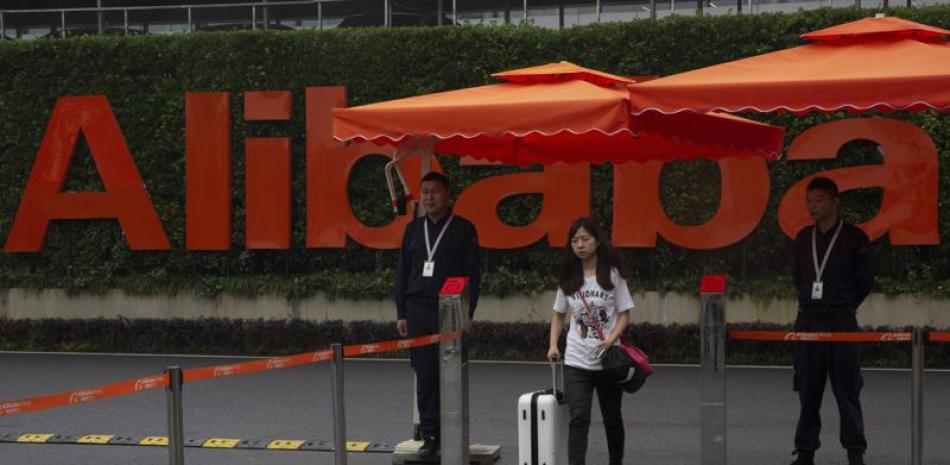 Una mujer lleva una maleta mientras pasa entre guardias de seguridad en la entrada de la sede de la compañía Alibaba en Hangzhou, en China, el 27 de mayo de 2016. (AP Foto/Ng Han Guan)