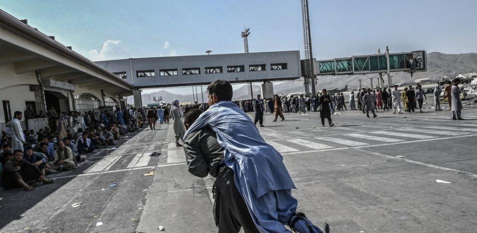 Un voluntario lleva a un hombre herido mientras se puede ver a otras personas esperando en el aeropuerto de Kabul en Kabul el 16 de agosto de 2021, después de un final asombrosamente rápido de la guerra de 20 años de Afganistán, mientras miles de personas asaltaron el aeropuerto de la ciudad tratando de huir del grupo. temía la línea dura de gobierno islamista. Wakil Kohsar / AFP