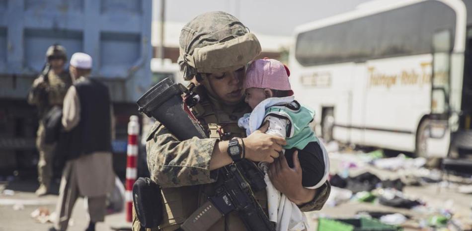 En esta imagen difundida por el Cuerpo de Marines de Estados Unidos, un elemento de la 24ta Unidad de Expedición carga a un bebé mientras se procesa a su familia en un centro de control de evacuación, el sábado 28 de agosto de 2021, en el Aeropuerto Internacional Hamid Karzai, de Kabul. (Staff Sgt. Victor Mancilla/U.S. Marine Corps via AP)