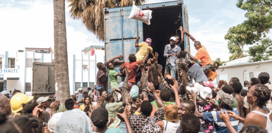 Un hombre arroja una bolsa de arroz a una multitud de víctimas del terremoto reunidas para la distribución de alimentos y agua en el cruce de “4 Chemins” en Les Cayes, Haití. Bandas criminales fuertemente armadas controlan varios suburbios de Puerto Príncipe, donde llevan a cabo secuestros y dificultan la entrega de ayuda humanitaria. / AFP