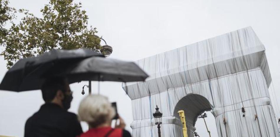 Dos personas miran cómo varios trabajadores envuelven en tela el monumento del Arco de Triunfo | AP